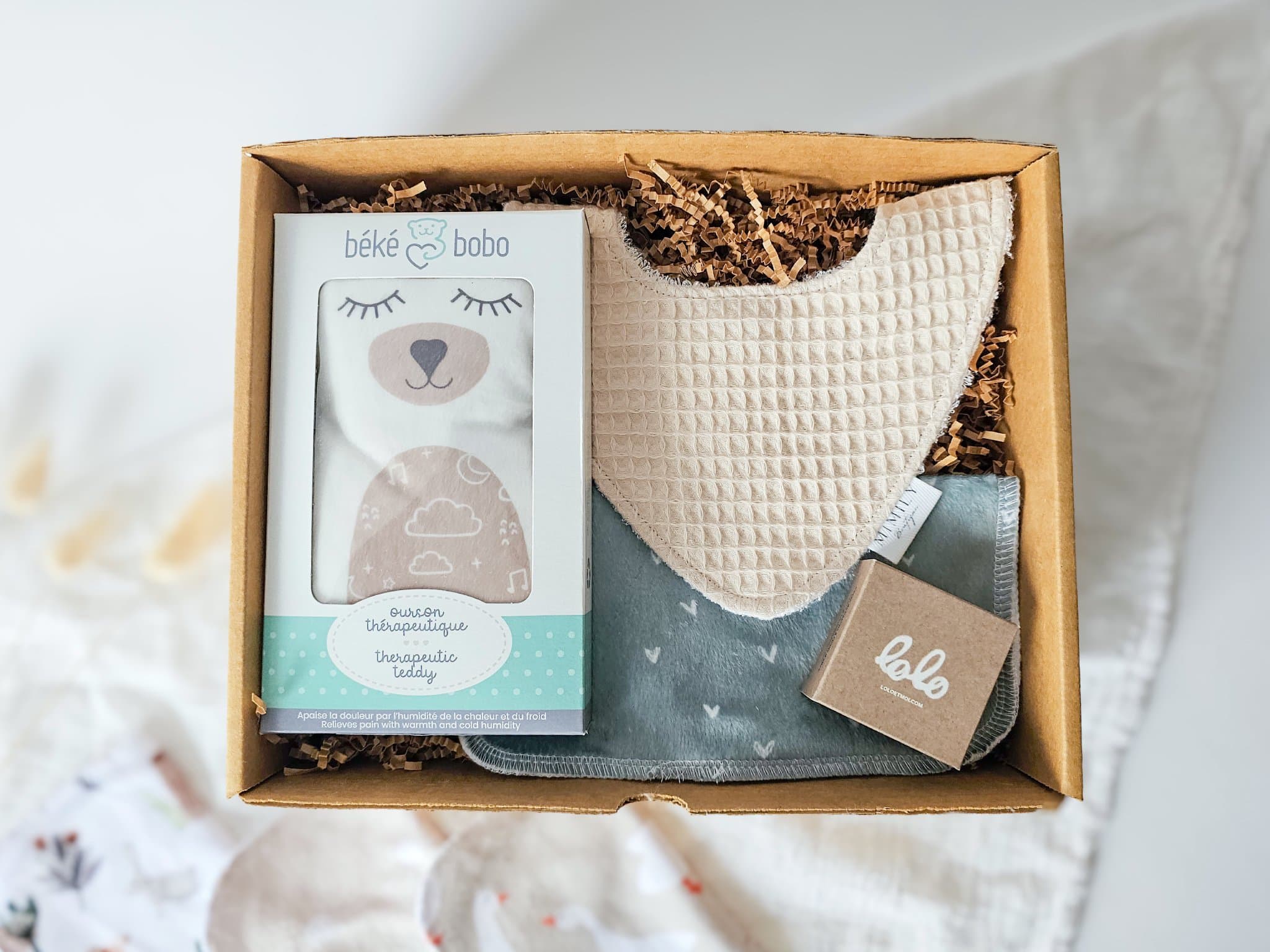 Boîte Petit trésor vue du dessus avec ourson thérapeutique Béké bobo, bavoir absorbant, débarbouillette douce et savon naturel, un ensemble pratique et réconfortant pour bébé.